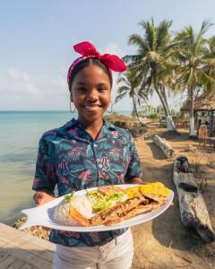 a woman holding a plate of food on the beach at La Playita Isla Fuerte in Puerto Limón