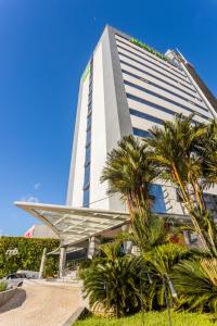 a tall white building with palm trees in front of it at Ibis Styles Belém Hangar in Belém