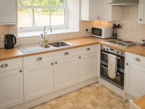 cocina con armarios blancos, fregadero y microondas en Uk35715 - South Cottage en Teviothead