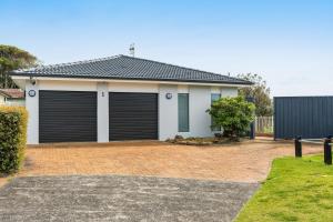 a house with two garage doors on a brick driveway at Norah Head Seascape in Norah