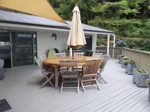 einem Holztisch mit Stühlen und einem Sonnenschirm auf einer Terrasse in der Unterkunft Water's Edge Holiday Home in Opua