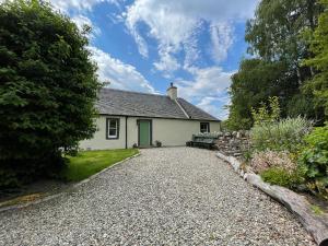 a small white house with a gravel driveway at Old Manse Cottage in Auchterneed