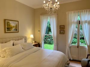 a bedroom with a bed with a chandelier and two windows at Rowan Brae Historic Guesthouse in Blackheath