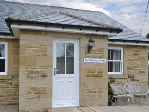 a cottage with a white door and a stone wall at No 2 Railway Cuttings - Uk3402 in Falstone