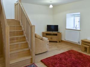 a living room with a staircase with a chair and a television at Stabal Rhoswen in Ffestiniog