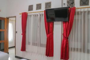 uma televisão pendurada numa parede com cortinas vermelhas em Wisma Vandera Syariah Garut Mitra RedDoorz em Garut