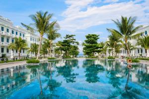 a large swimming pool with palm trees in front of a building at 8BR West coast Phu Quoc townhouse by beach and shared swimming pools in Phú Quốc