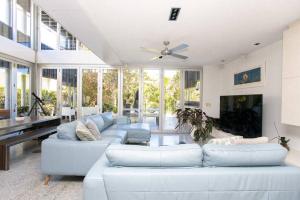Casuarina Beachfront House - Hostie Properties في ساحة كاسوارينا: غرفة معيشة مع أرائك بيضاء ومروحة سقف