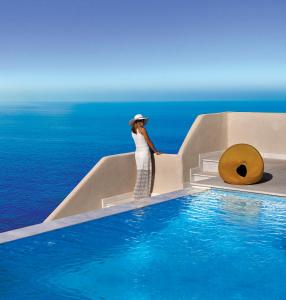 a woman in a white dress standing next to a swimming pool at Out Of The Blue Resort & Spa in Agia Pelagia