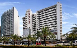 un gran edificio blanco con palmeras y autobuses en Ramada Plaza by Wyndham Sanya Bay en Sanya