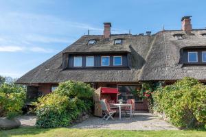 a house with a thatched roof with a table and chairs at Bens Hüs in Braderup