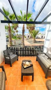 un patio con sillas, mesas y palmeras en Casa Ayla Montecastillo A8, en Caleta de Fuste