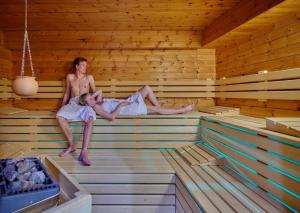 Ein Mann und eine Frau sitzen in einer Sauna in der Unterkunft Hotel Restaurant Zum Goldenen Anker mit Hallenbad & Wellnessbereich in Windorf
