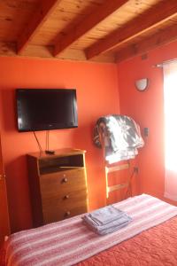 1 dormitorio con pared de color naranja y TV de pantalla plana en cabaña en Pichilemu, en Pichilemu