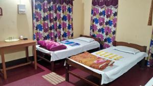 two beds in a room with a desk and curtains at Subansiri lodge in Majuli +5 photos
