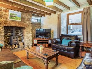 a living room with leather furniture and a stone fireplace at Rescorla Cottage in Penwithick