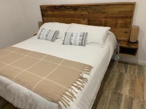 uma cama com lençóis brancos e almofadas num quarto em Cabañas El jardín de Jacinta em Coihaique