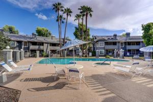 a pool with chairs and umbrellas in front of a house at Pet-Friendly Condo with Pool about 7 Mi to Dtwn Chandler in Chandler
