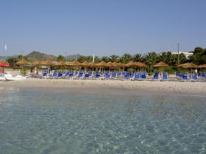 a beach with blue chairs and umbrellas and the water at Hotel Simius Playa in Villasimius