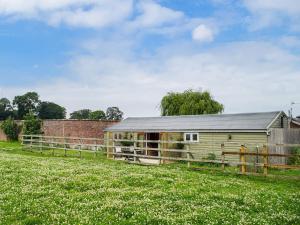 a green barn in a field with a fence at The Summerhouse - Uk34933 in Baschurch