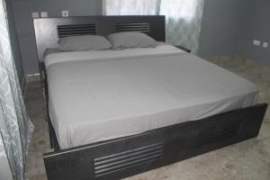 a bed with a black frame and white sheets at Coast to Coast Vacation Home in Winneba