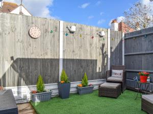 a backyard with a wooden fence with plants and a clock at La Casita in Herne Bay
