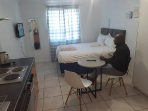 een man aan een tafel voor een bed bij Durham Square Apartments in Kaapstad
