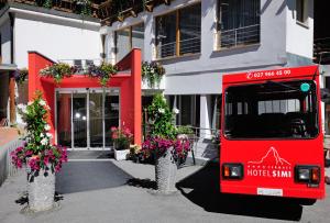 un autobus rosso parcheggiato di fronte a un edificio con fiori di Hotel Simi a Zermatt