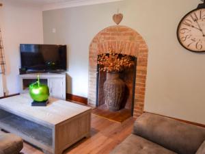 a living room with a brick fireplace and a clock at Tree Tops Cottage in Mundford