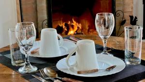 a table with plates and wine glasses and a fireplace at Chalé Vila do Aeroporto in Monte Verde