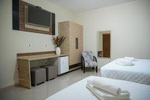 a room with two beds and a desk and a tv at Hotel Camburi Praia in Camburi