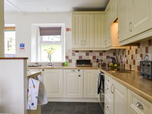 a kitchen with white cabinets and a window at Greve Cottage in Marykirk