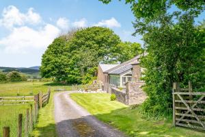 a stone house on a dirt road next to a fence at Pickle Cottage in Carnforth