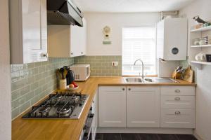 una cucina con armadi bianchi e piano cottura di Duck Cottage - Pet-friendly Traditional Rural Home a Kilrenny