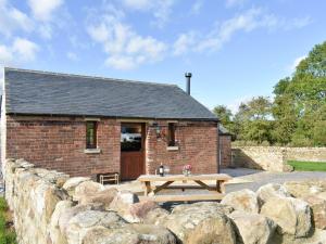 a brick building with a picnic table next to a stone wall at Shepherds Den in Crakehall