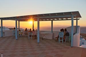 um grupo de pessoas sentadas num telhado a ver o pôr-do-sol em Aethrio Sunset Village - Oia em Oia