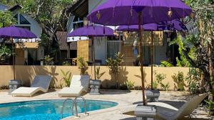 a pool with chairs and purple umbrellas next to a building at Teratai Boutique Resort in Amed