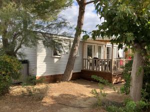a small white house with a porch and a tree at Mobil Home - Camping La Falaise in Narbonne