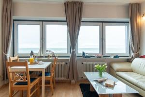 ein Wohnzimmer mit einem Tisch und einigen Fenstern in der Unterkunft "Strandhotel Heiligenhafen", Wohnung 317 "Seestern" (Typ II) in Heiligenhafen