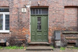 een groene deur aan de zijkant van een bakstenen gebouw bij House Of Malgosia in Gdańsk