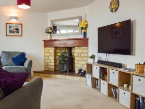 uma sala de estar com lareira e televisão em Primrose Cottage em Little Rissington