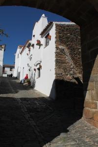 un bâtiment blanc avec un mur en pierre et une personne assise au sol dans l'établissement Casa Dom Dinis, à Monsaraz
