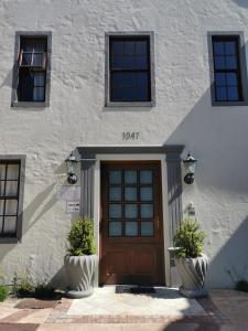 a white building with a wooden door and two plants at Blouberg Manor in Bloubergstrand