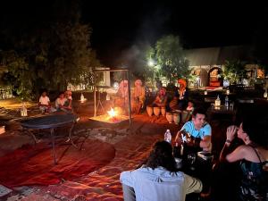 grupa ludzi siedzących w nocy przy ogniu w obiekcie Luxury traditional Tent Camp w mieście Merzouga
