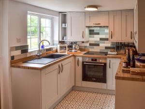 a kitchen with white cabinets and a sink and a window at Fox Cottage in Henstead