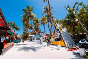 a beach with palm trees and a yellow building at Alaika Maafushi in Maafushi