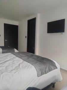 1 dormitorio con 2 camas y TV de pantalla plana en la pared en Hotel Cacique, en Duitama