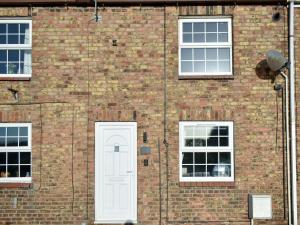 a brick building with a white door and three windows at Cernunnos Cottage in Leven