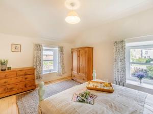 a bedroom with a bed and a dresser and two windows at Wrens Beck Cottage in Ousby