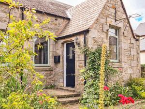 a stone house with a black door and some flowers at The Old School in Lowick